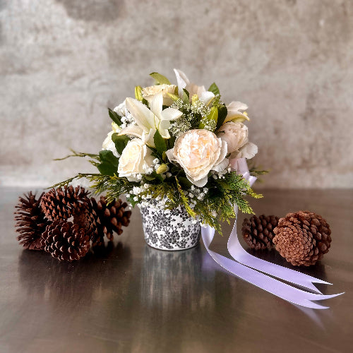 Norway Scandinavian Christmas arrangement with white lilies, champagne garden roses, cypress foliage and white accent flowers in a black and white patterned pot with lilac ribbon.