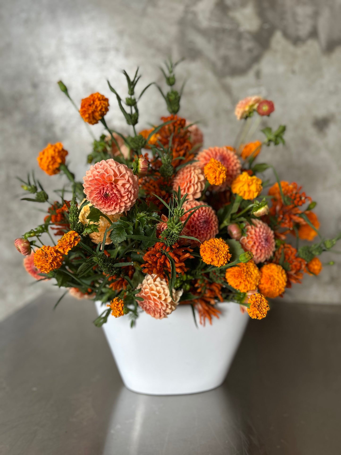 Turin bold elegance arrangement in radiant orange and soft peach tones, sculptural and textural, presented in a contemporary white vessel. Vessel may vary.